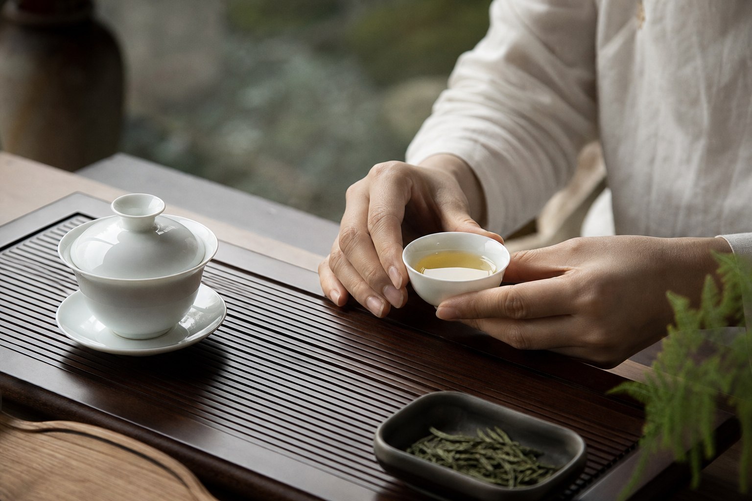 手捧白瓷小杯品饮绿茶